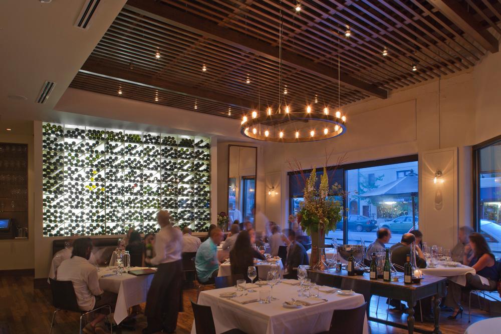 Dimly lit dining room in a kitchen with many patrons and wine wall