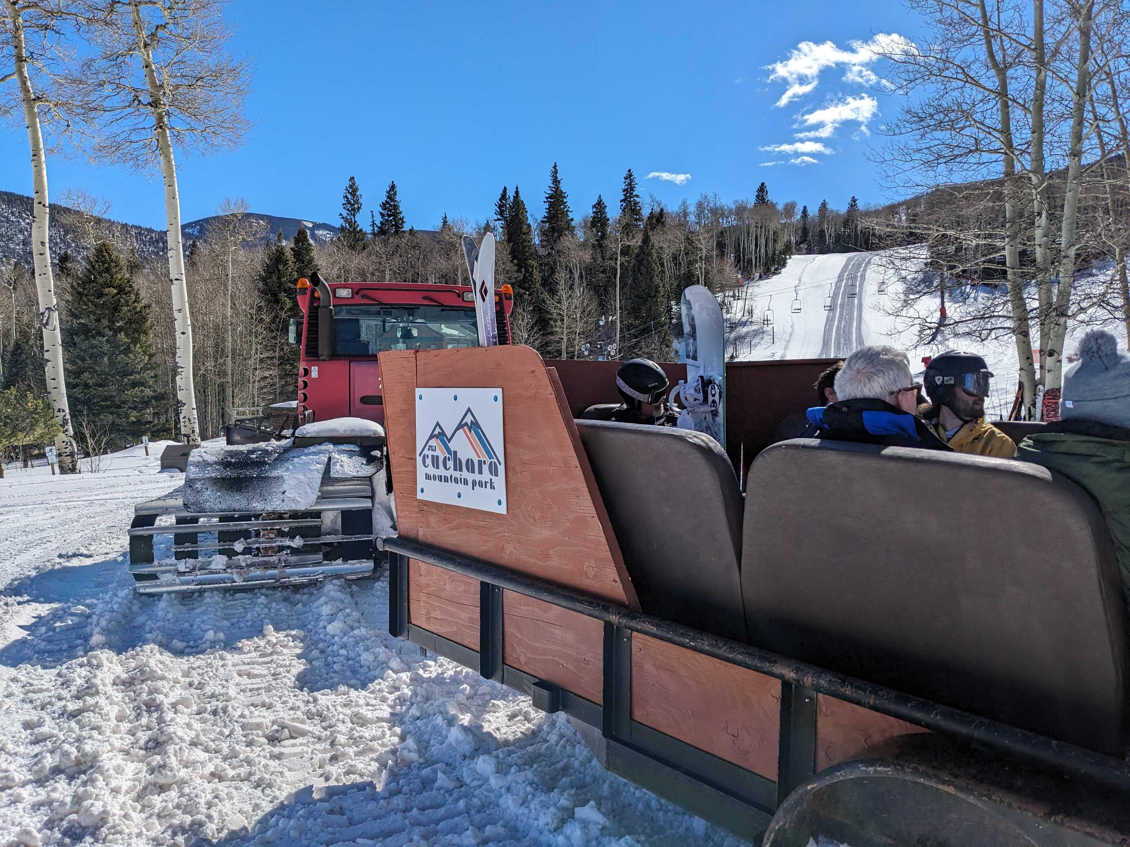 skiers and boarders sit in a trailer sled attached to a snow cat