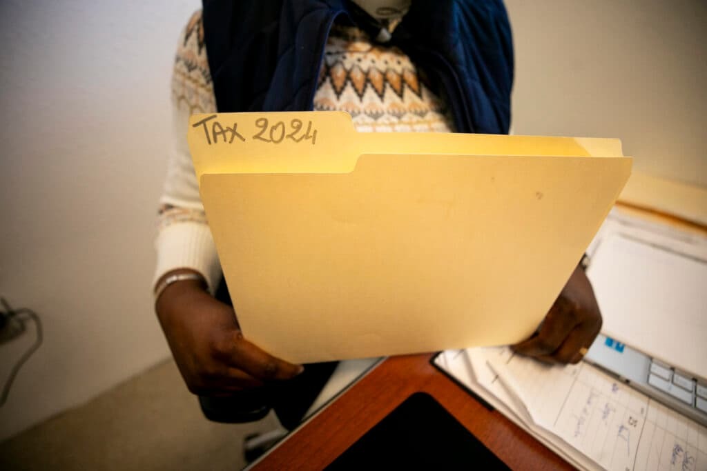 A woman holds a manila folder titled "TAX 2024"