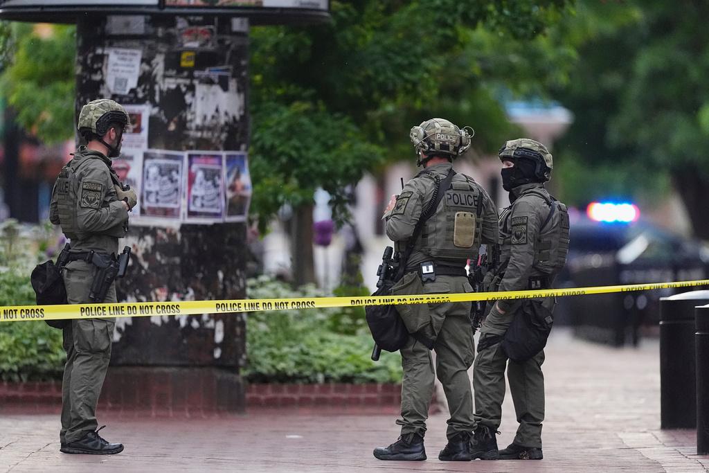 Three people in police uniforms stand behind yellow police tape